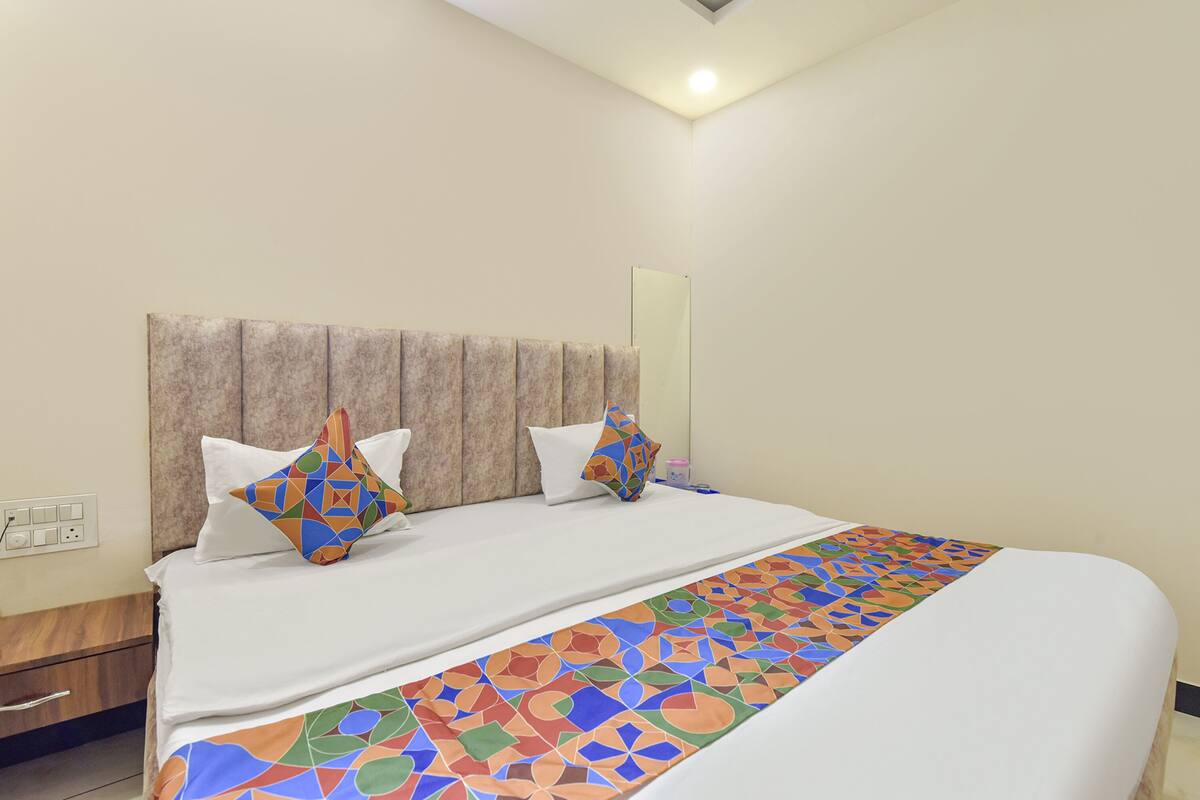 A neatly made bed with a patterned runner, a wooden nightstand, and a wall-mounted mirror.