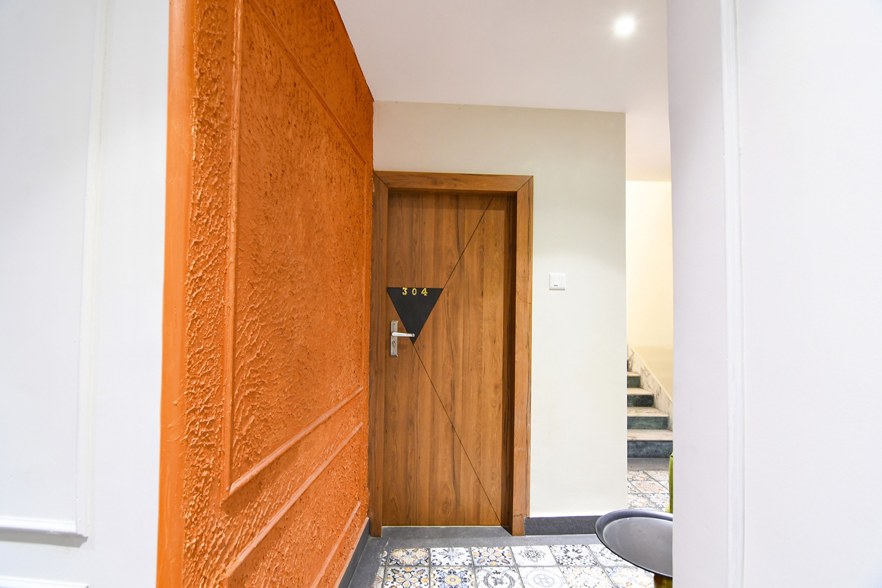 A hallway with a wooden door marked with the number 304, a tiled floor, and a staircase in the background.