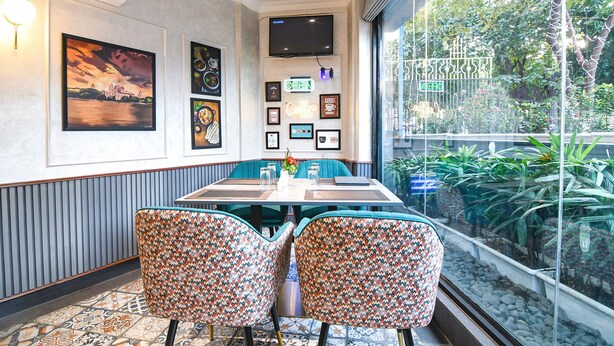 Een eetgedeelte met een grote tafel, twee gestreepte stoelen, ingelijste foto’s aan de muur en uitzicht op groen door een glazen raam.