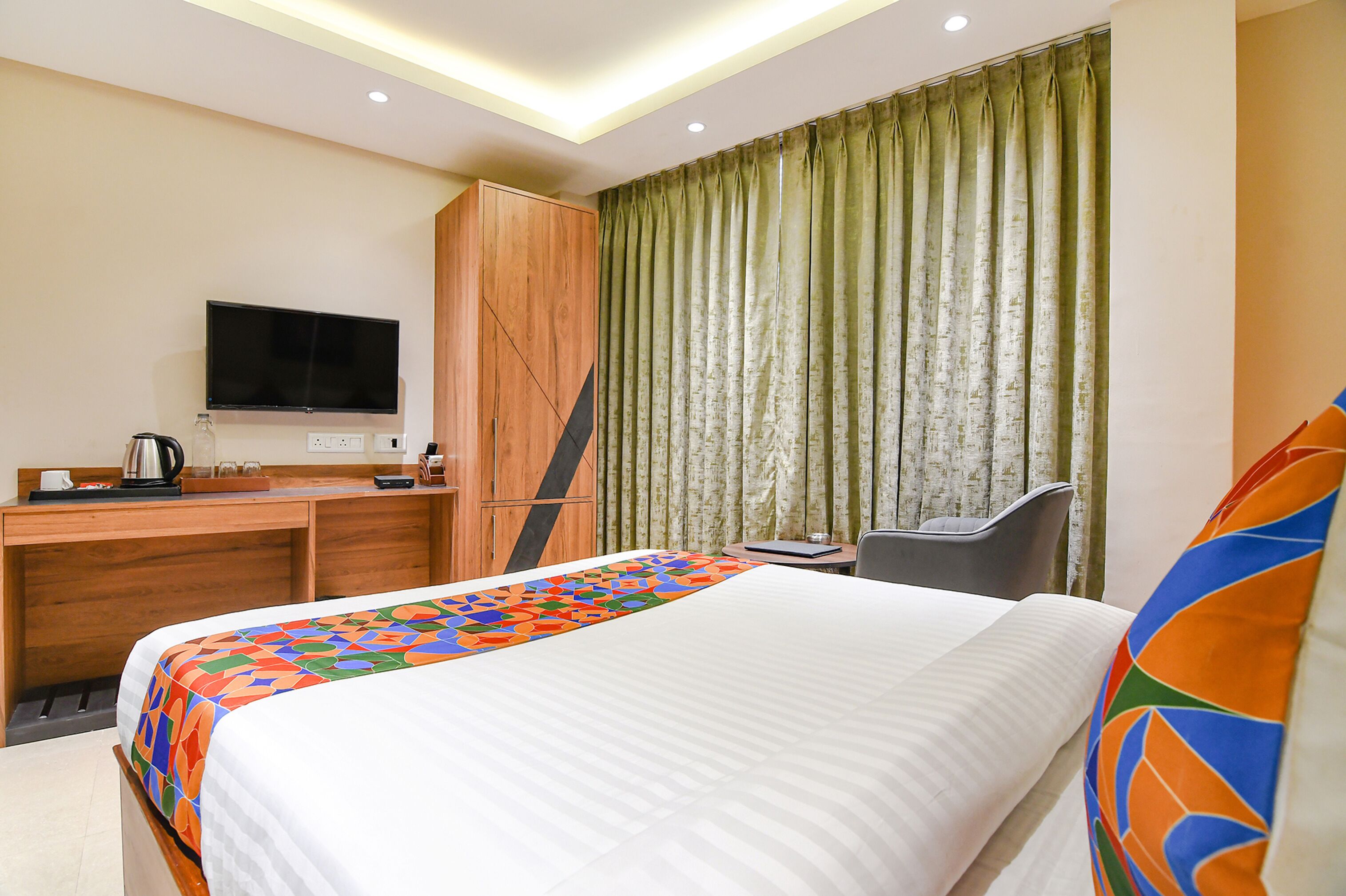 A hotel room with a bed, a desk, a chair, a television, and a window with curtains.