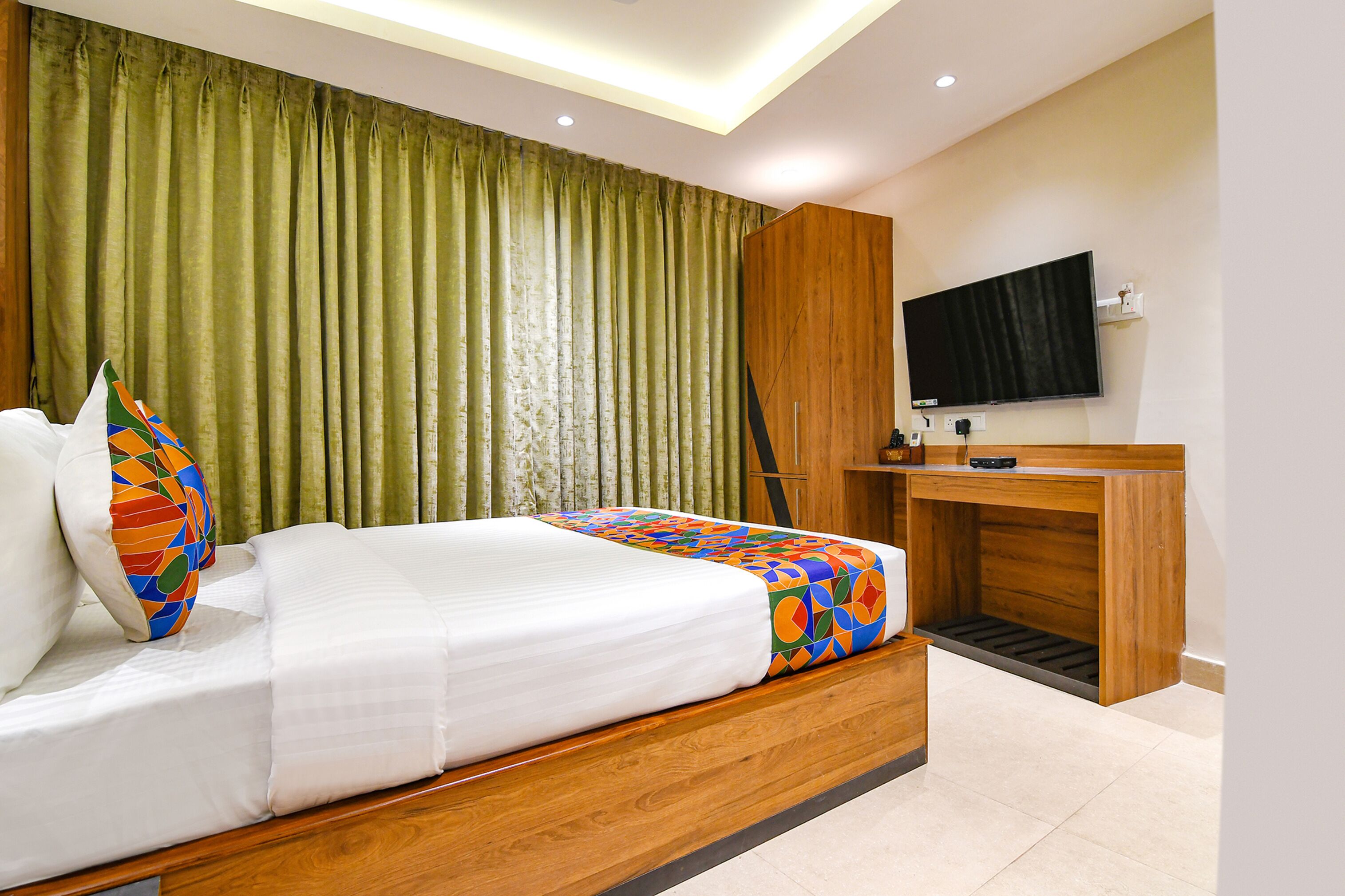 A modern hotel room with a wooden bed, a television, and a desk with a chair.