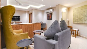Een moderne woonkamer met een bank, een gele fauteuil, een klein rond tafeltje en een aan de muur bevestigde televisie.