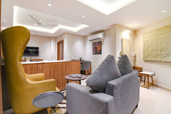 A modern living room with a sofa, a yellow armchair, a small round table, and a TV mounted on the wall.