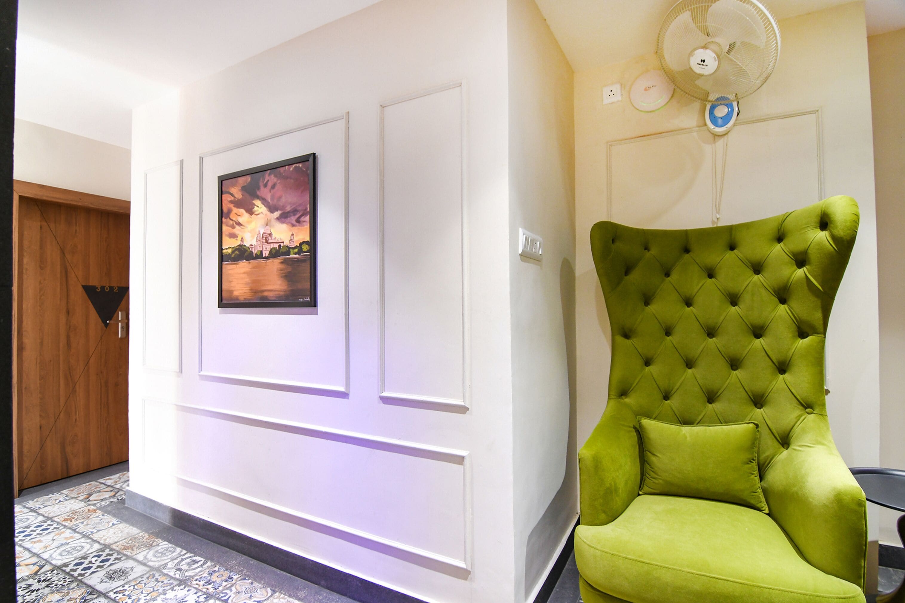 Une pièce avec un fauteuil à revêtement vert, un tableau encadré au mur et une porte blanche.