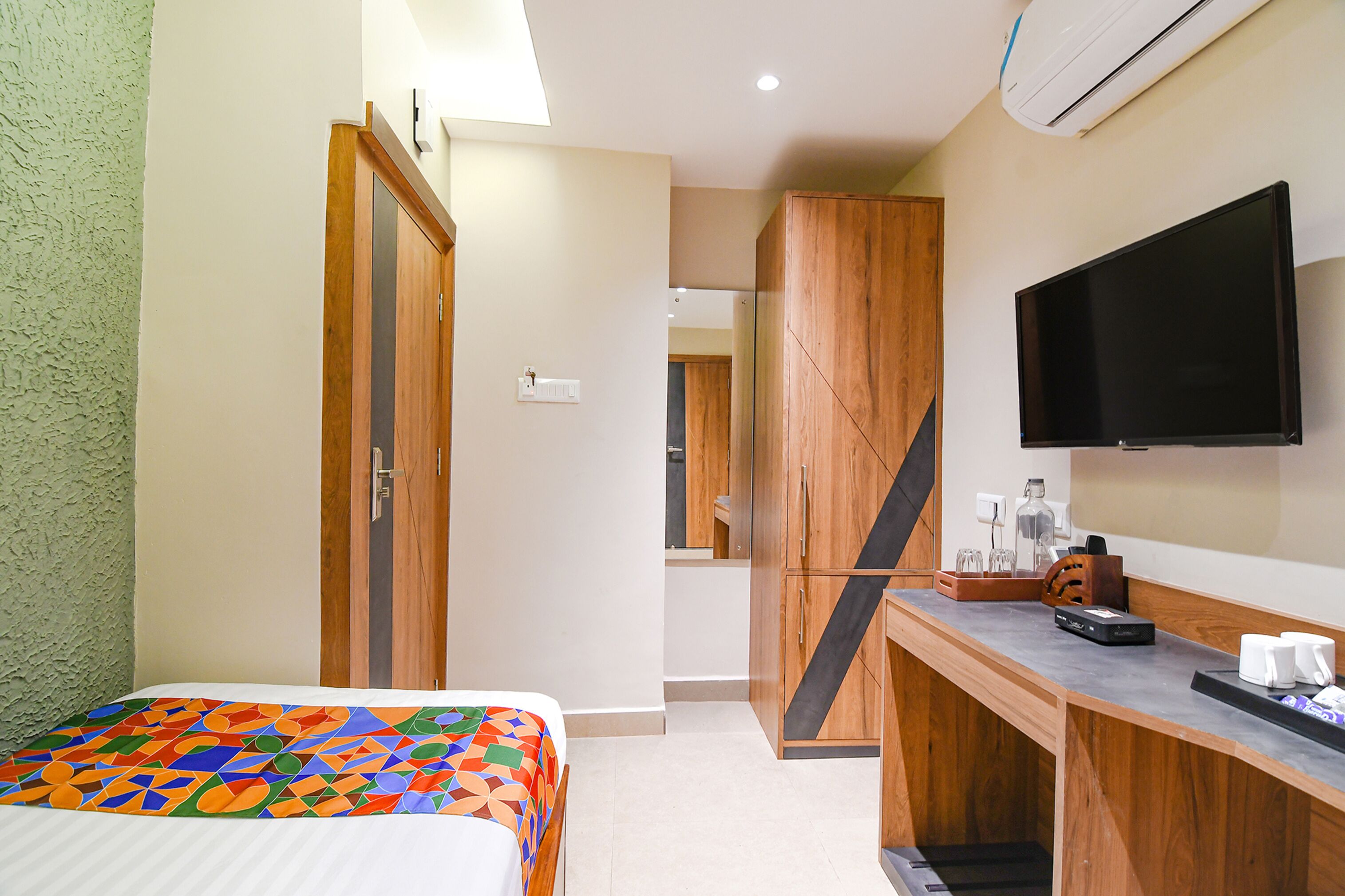 Une chambre d’hôtel comprenant un lit, une armoire en bois, un bureau avec un téléviseur à écran plat et un coin café.