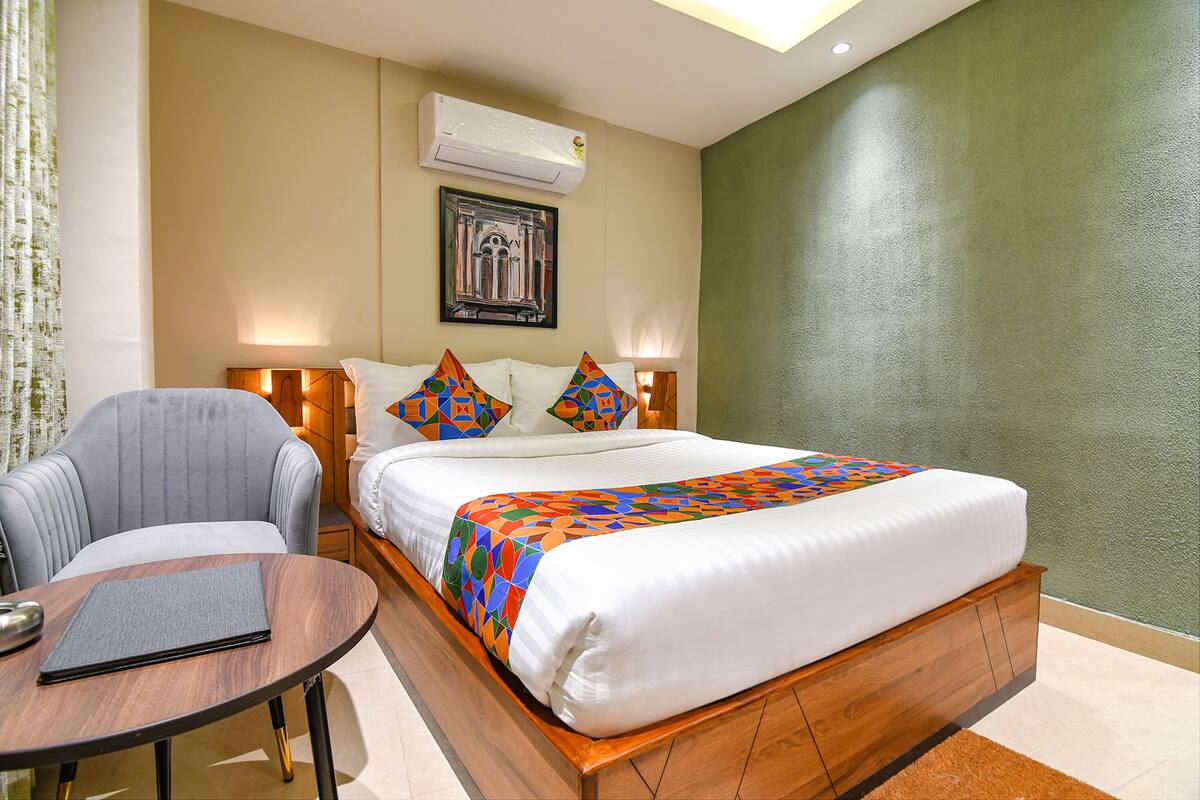 Ein Hotelzimmer mit Bett, Sessel, kleinem Tisch, Klimaanlage und einem gerahmten Bild an der Wand.