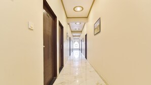 Un couloir d’hôtel avec un sol en marbre, des portes en bois et un éclairage encastré.