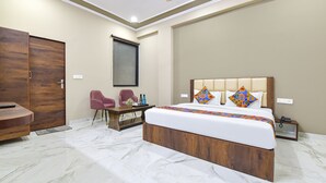 Une chambre d’hôtel moderne avec un grand lit, une tête de lit en bois et un bureau avec des chaises.