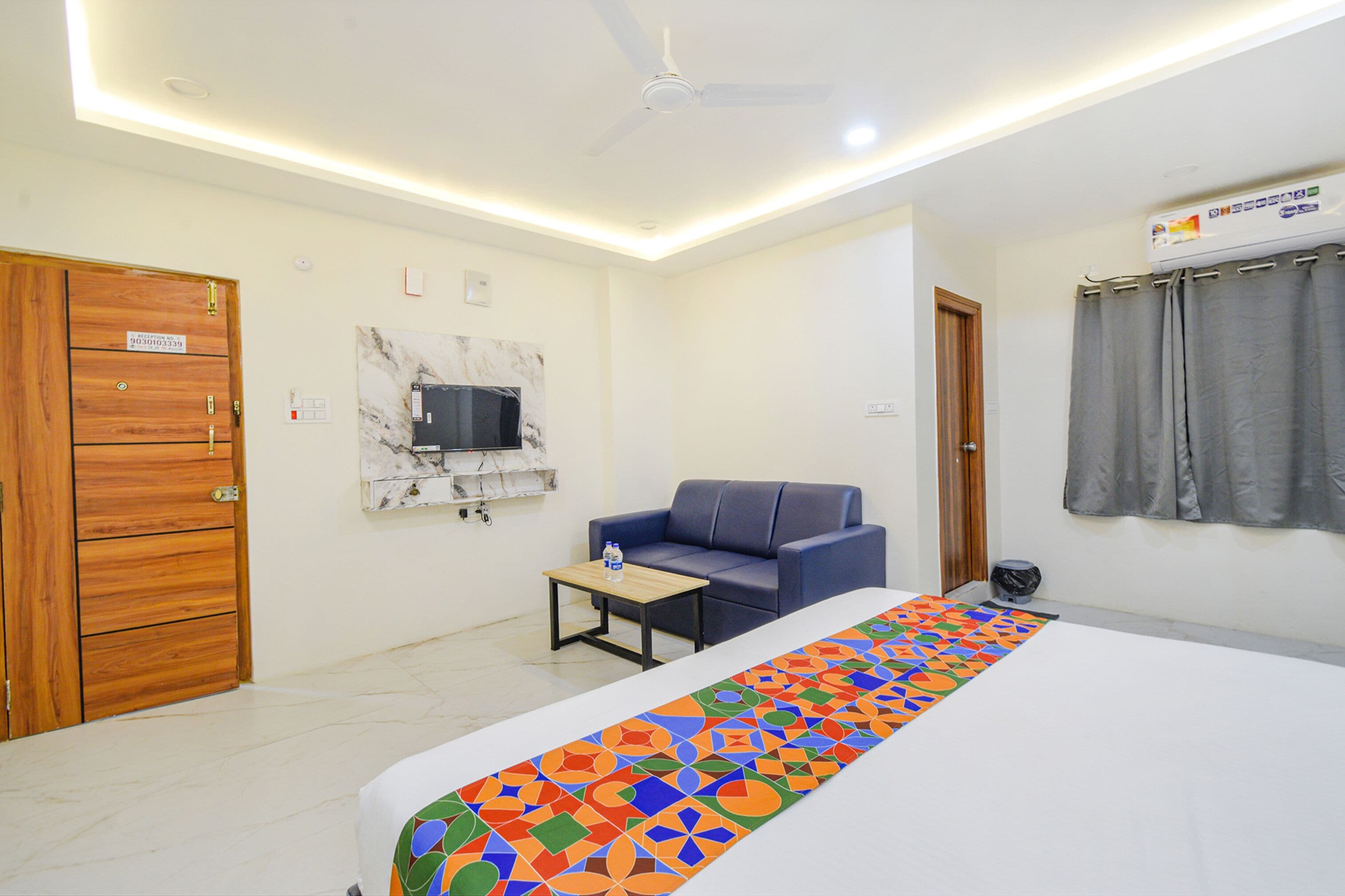 Habitación de hotel con cama, sofá, una mesita, televisor y ventilador de techo.