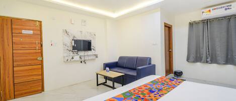 Habitación de hotel con cama, sofá, una mesita, televisor y ventilador de techo.