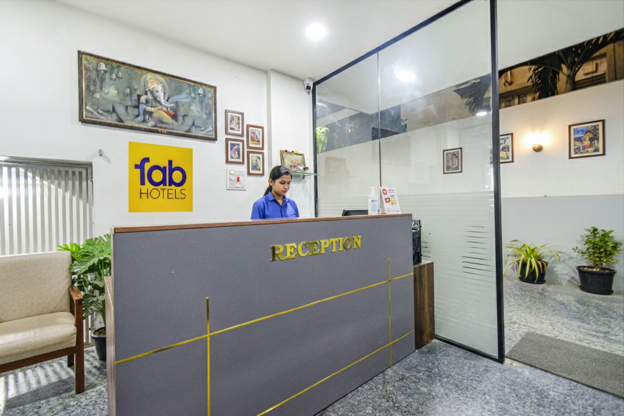 Un comptoir d’accueil avec une enseigne indiquant « fab hotels », des tableaux encadrés accrochés au mur et un réceptionniste.