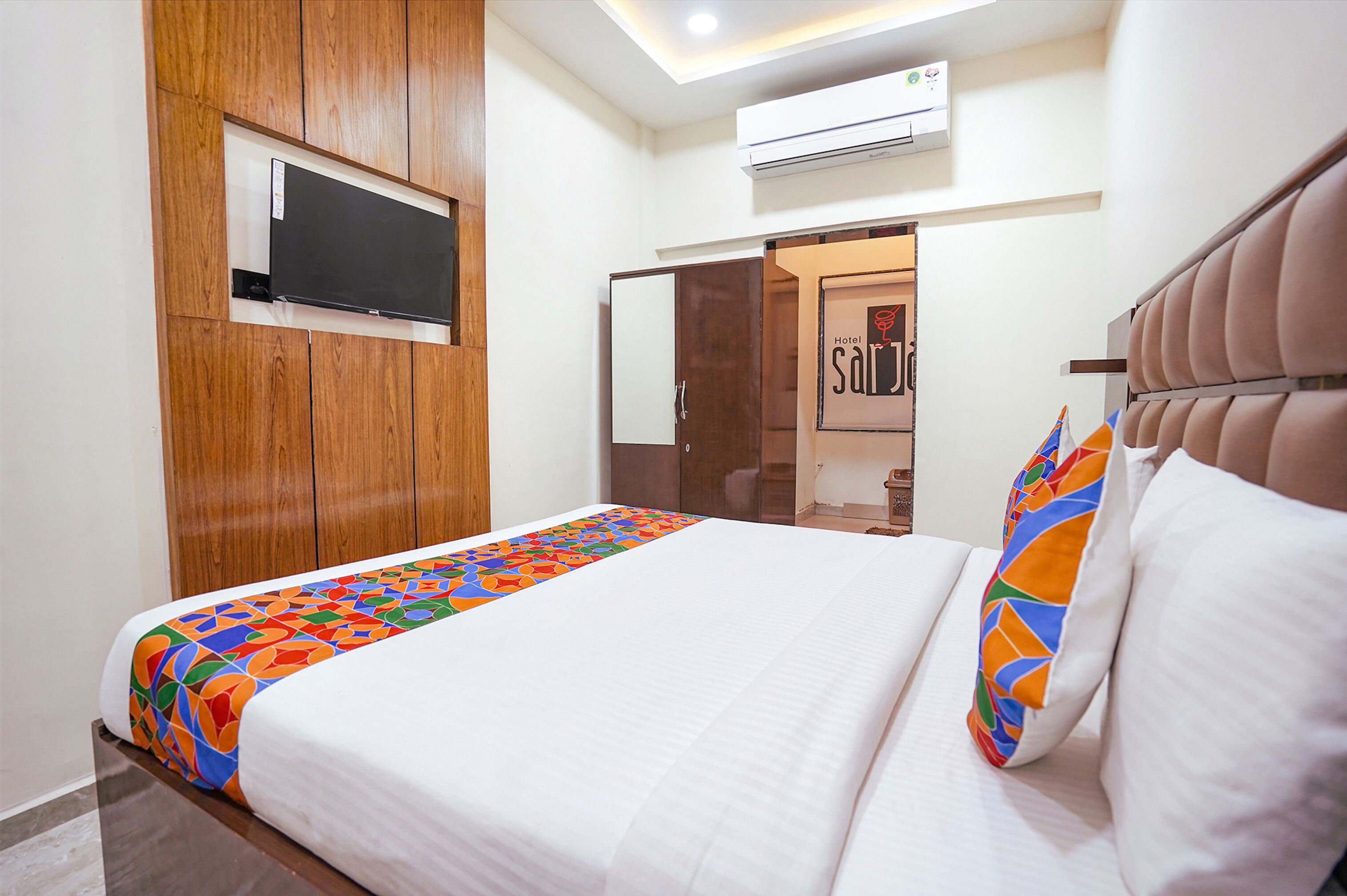 A hotel room with a bed, a TV mounted on the wall, and a door leading to a bathroom.