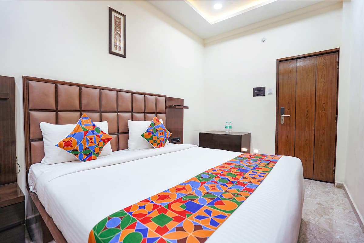Una cama bien hecha con un colorido edredón geométrico, un cabecero de madera y dos almohadones decorativos.
