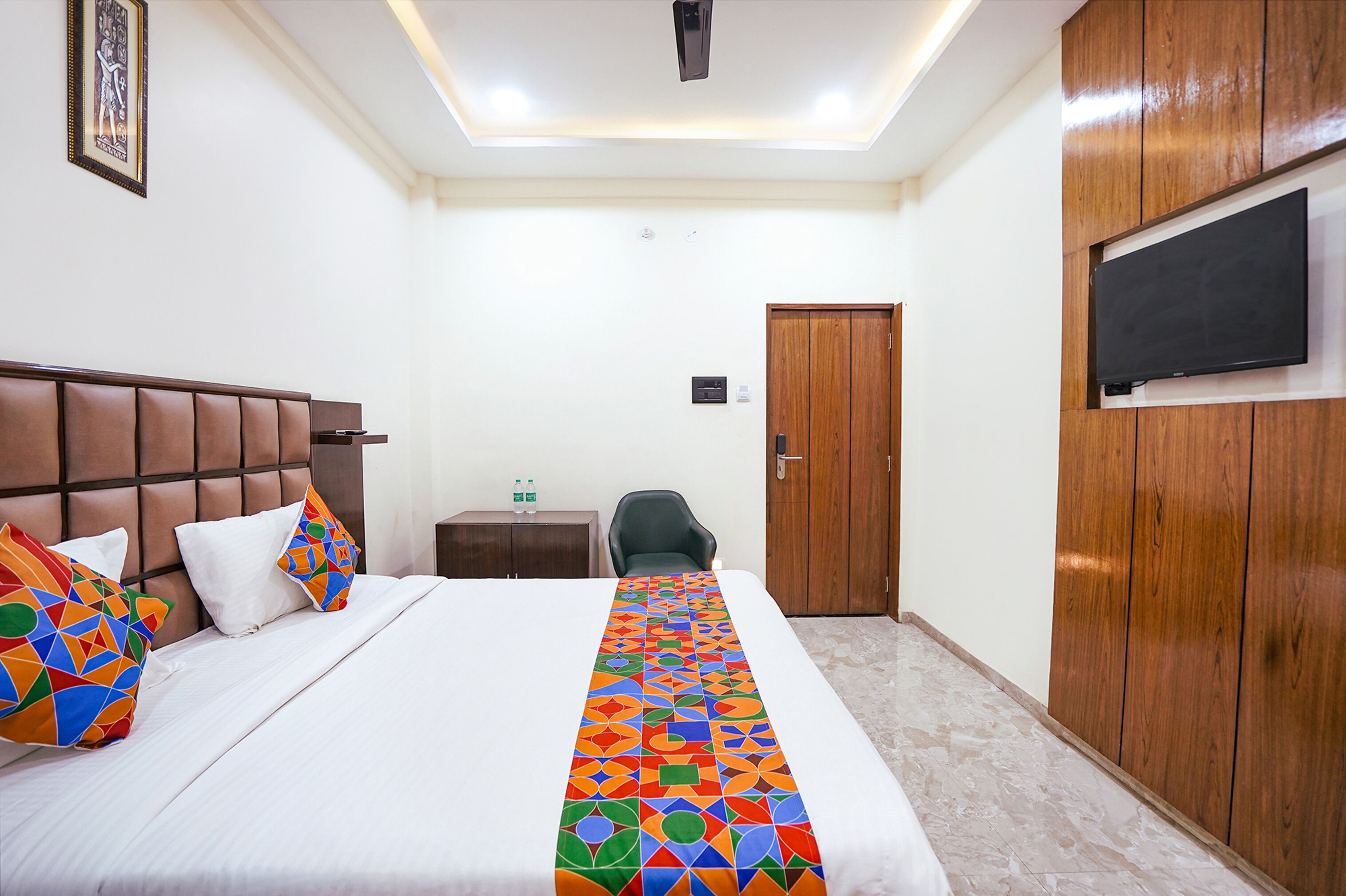 Una camera d'albergo con un letto grande, una testiera in legno, una TV a parete e una porta.