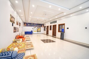 Un hall d’hôtel spacieux, doté d’un plafond haut, d’un éclairage encastré et d’un espace salon central agrémenté de coussins à motifs.