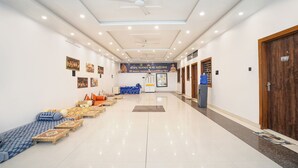 A hotel corridor with a polished floor, ceiling fans, and artwork on the walls. - Fabhotel Shree Radha Ashtami Seva Ashram (Mathura)