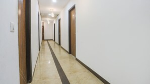 A long, narrow hallway with white walls and wooden doors, leading to multiple rooms. - Fabhotel Golden Key (New Delhi)