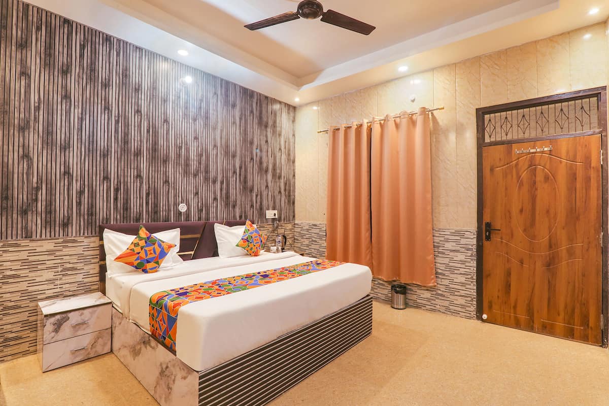 A modern hotel room with a large bed, a wooden headboard, a ceiling fan, and a wooden door.