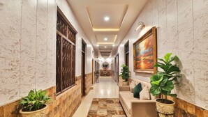 A hallway with patterned walls, a central bench, potted plants, and a painting on the wall. - Fabexpress Ramayana Premium (Faizabad)