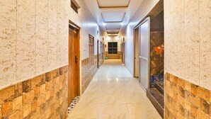 A hotel hallway with a marble floor, stone wall accents, and doors leading to rooms. - Fabexpress Ramayana Premium (Faizabad)