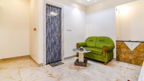 A room with a green sofa, a marble-tiled floor, a door labeled "WASH ROOM", and a cabinet with a marble finish. - Fabhotel City Star (Bidhannagar)