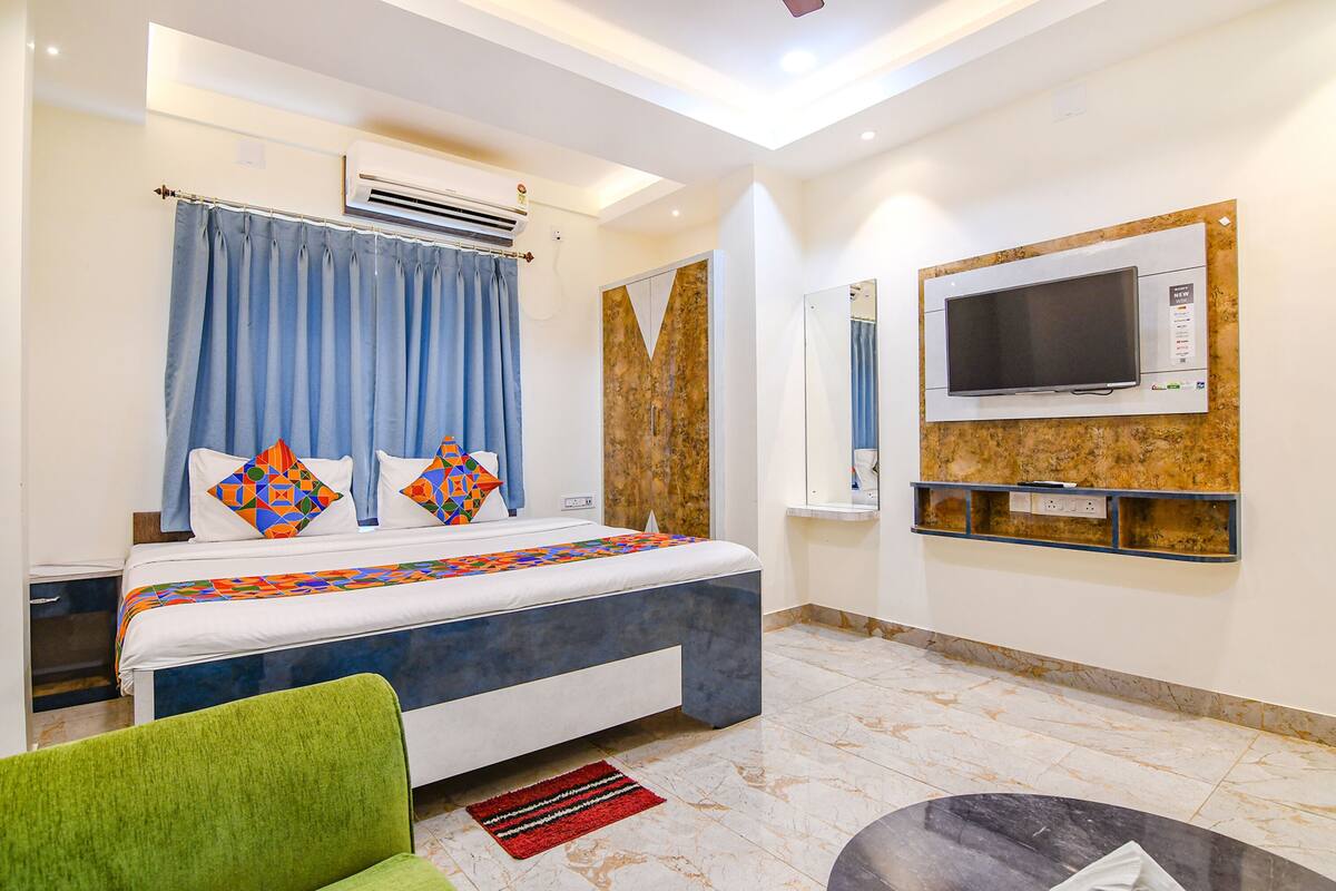 A modern hotel room with a bed, air conditioning unit, television, and a small seating area.