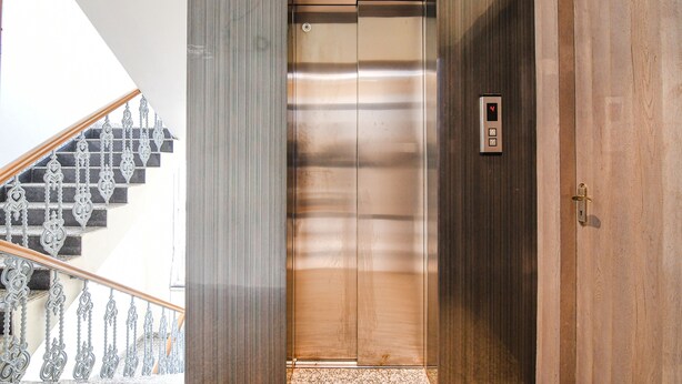An elevator with a digital display, a wooden door, and a staircase with ornate metal railings. - Fabhotel City Star (Bidhannagar)