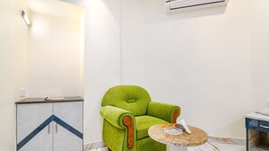 A room with a green armchair, a small round table, a cabinet with a geometric design, and an air conditioning unit on the wall. - Fabhotel City Star (Bidhannagar)