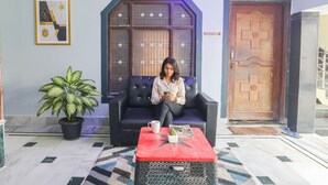 A room with a black leather sofa, a red coffee table, a potted plant, and a wooden door. - Fabhotel Awadh Inn - 600 m from Ram mandir (Ayodhya)