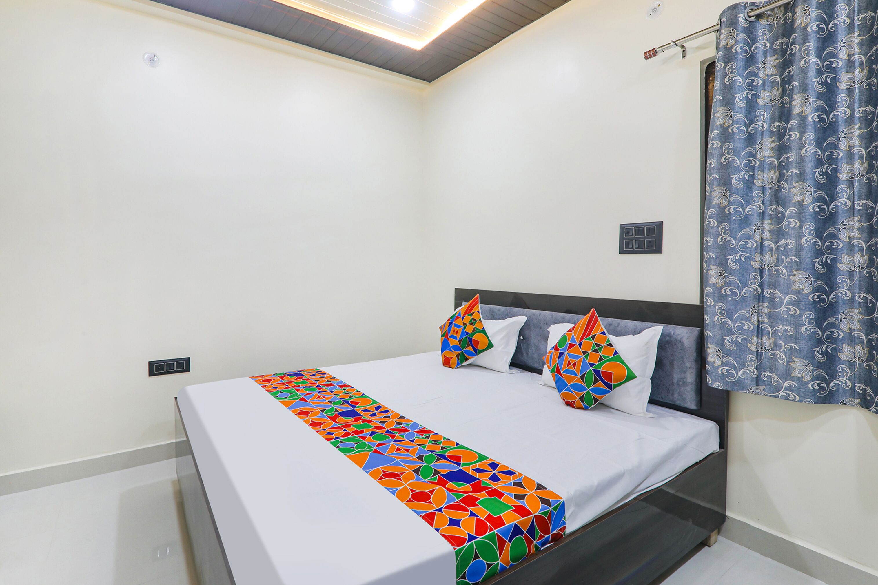 Una cama bien hecha con una colcha de diseño geométrico y colores vivos, un cabecero oscuro y dos almohadones decorativos.