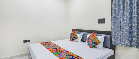 Una cama bien hecha con una colcha de diseño geométrico y colores vivos, un cabecero oscuro y dos almohadones decorativos.