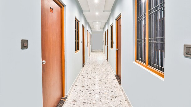 A hallway with wooden doors, a terrazzo floor, and a window with metal bars. - Fabexpress Atithi Niwas (Ayodhya)