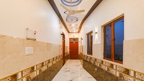 A hallway with a marble floor, decorative borders, a ceiling fan, and a door at the end. - Fabexpress Shree Siya Raman (Ayodhya)