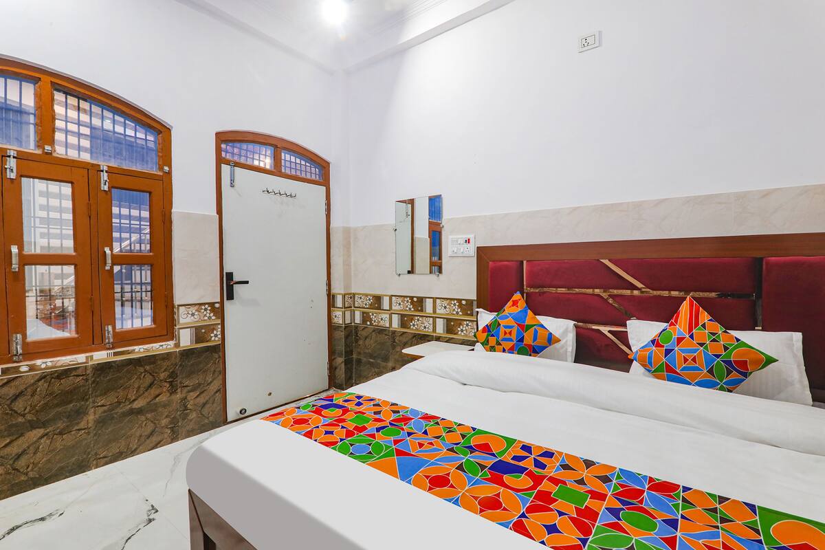 A hotel room with a bed, a door, a mirror, and a window with wooden frames.