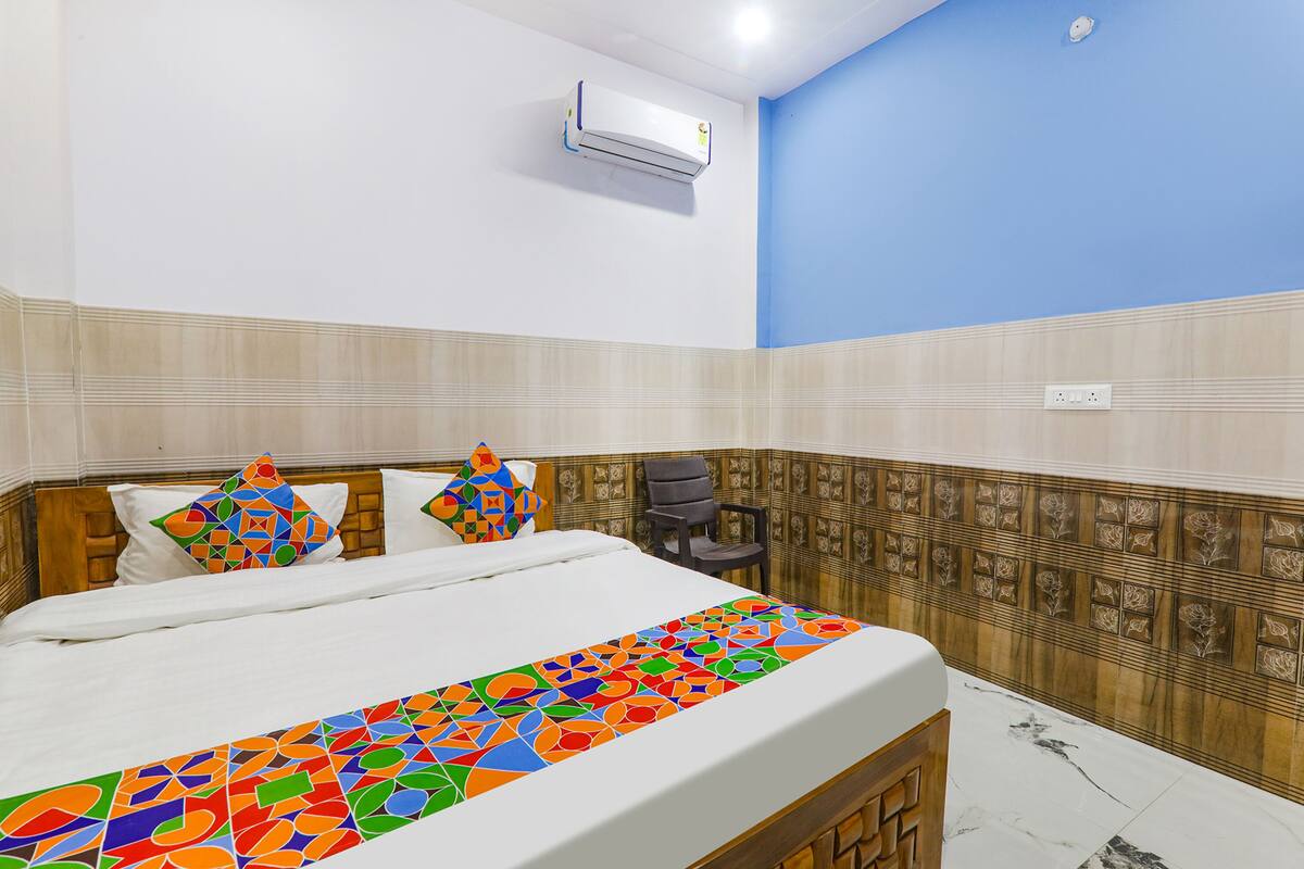 A hotel room with a bed, colorful pillows, a chair, a wall-mounted air conditioner, and patterned wall tiles.