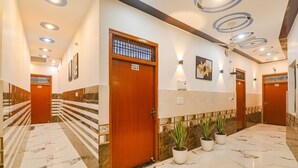 A hotel hallway with marble flooring, wooden doors, and potted plants. - Fabexpress Shree Siya Raman (Ayodhya)