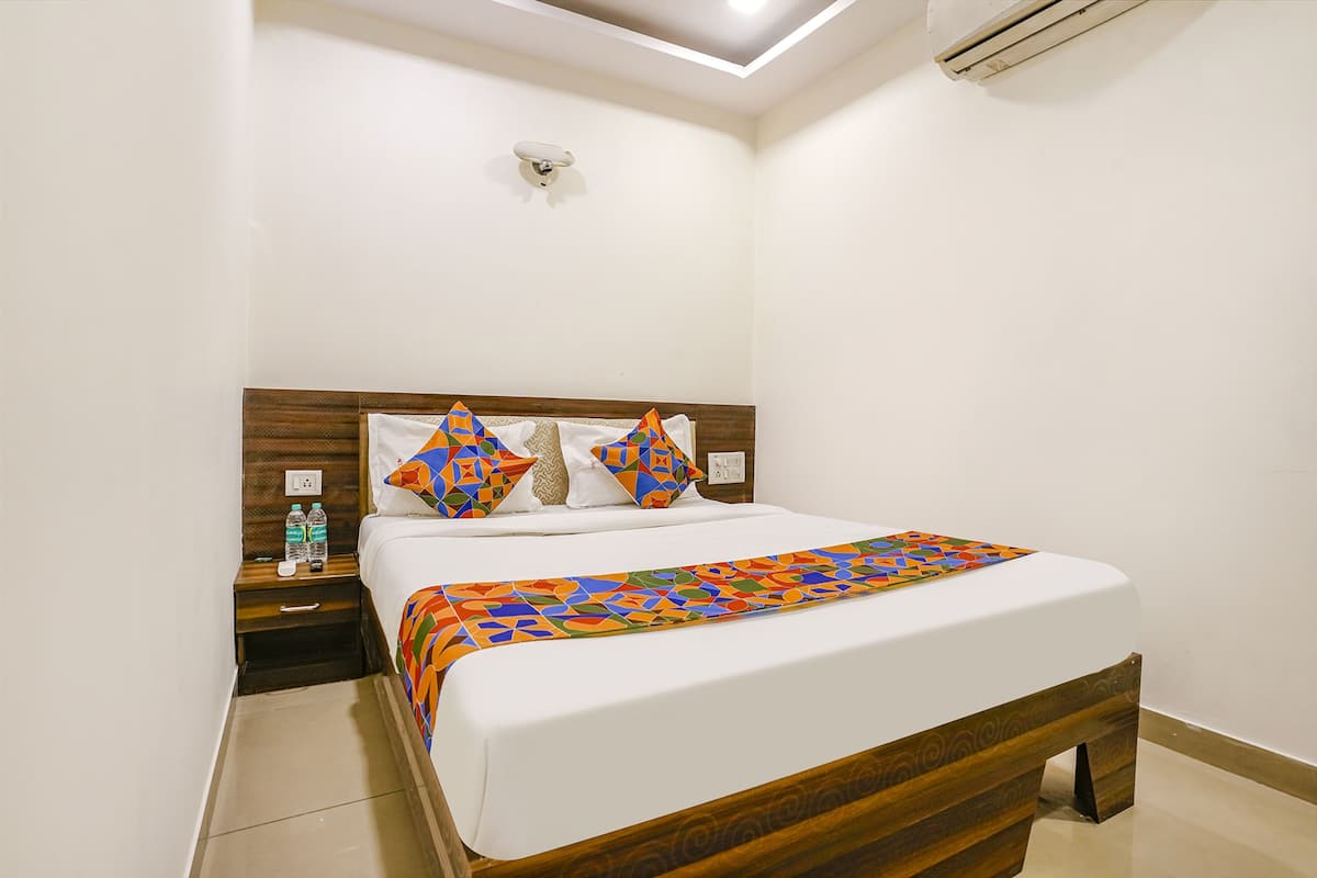 A neatly made bed with a geometric-patterned bedspread, a wooden headboard, and a nightstand with two water bottles.