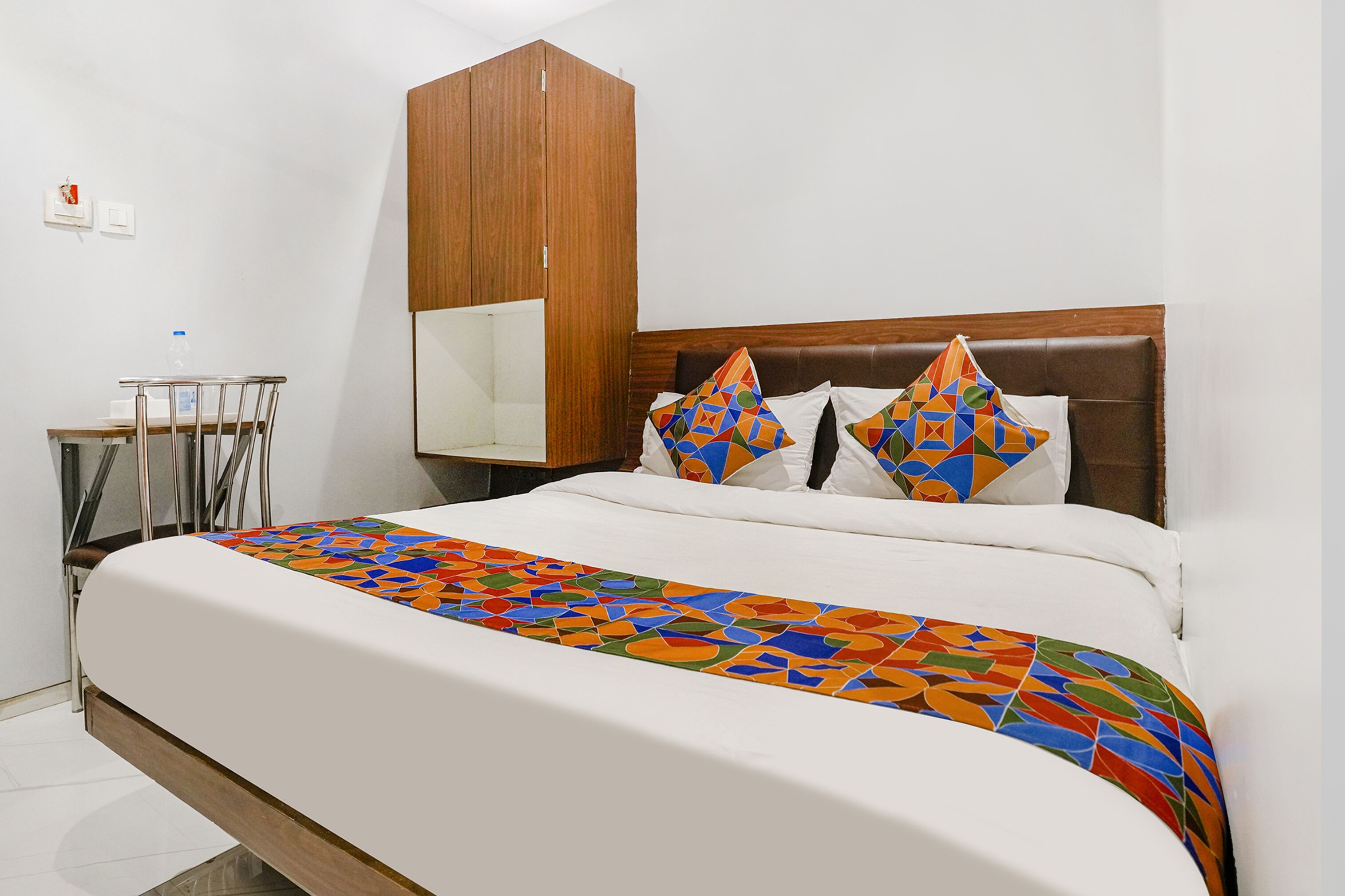 A neatly made bed with a colorful geometric-patterned bedspread, a wooden headboard, and two decorative pillows.