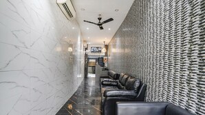 A hallway with a marble floor, black leather seating, a ceiling fan, and a textured wall. - Fabhotel Powai Inn (Mumbai)