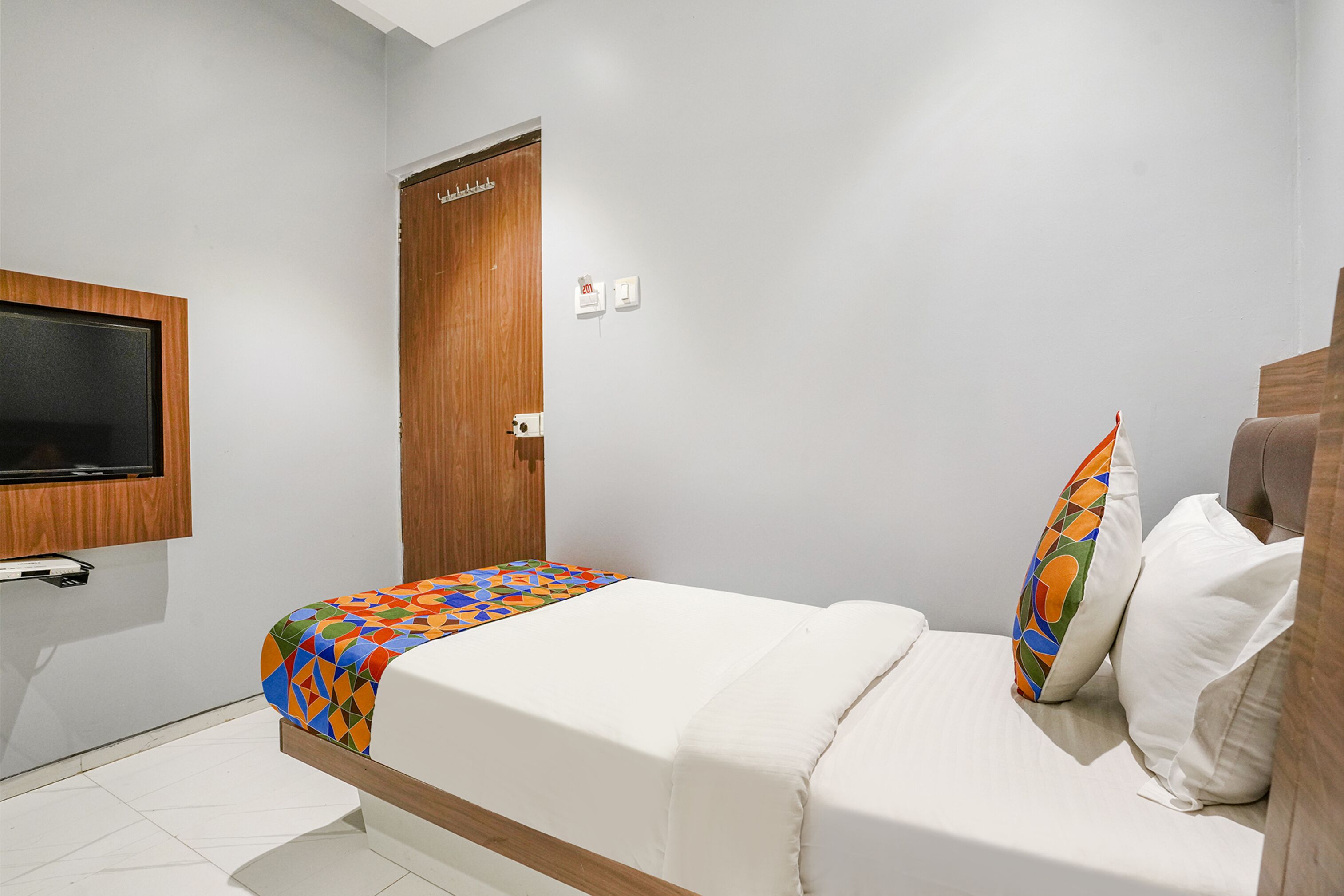 Ein Hotelzimmer mit einem Bett, einem an der Wand befestigten Fernseher, einer Holztür und einer weißen Wand.