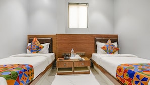 A double room with two beds, a wooden headboard, a small bedside table with a bottle, glasses, and a phone. - Fabhotel Powai Inn (Mumbai)