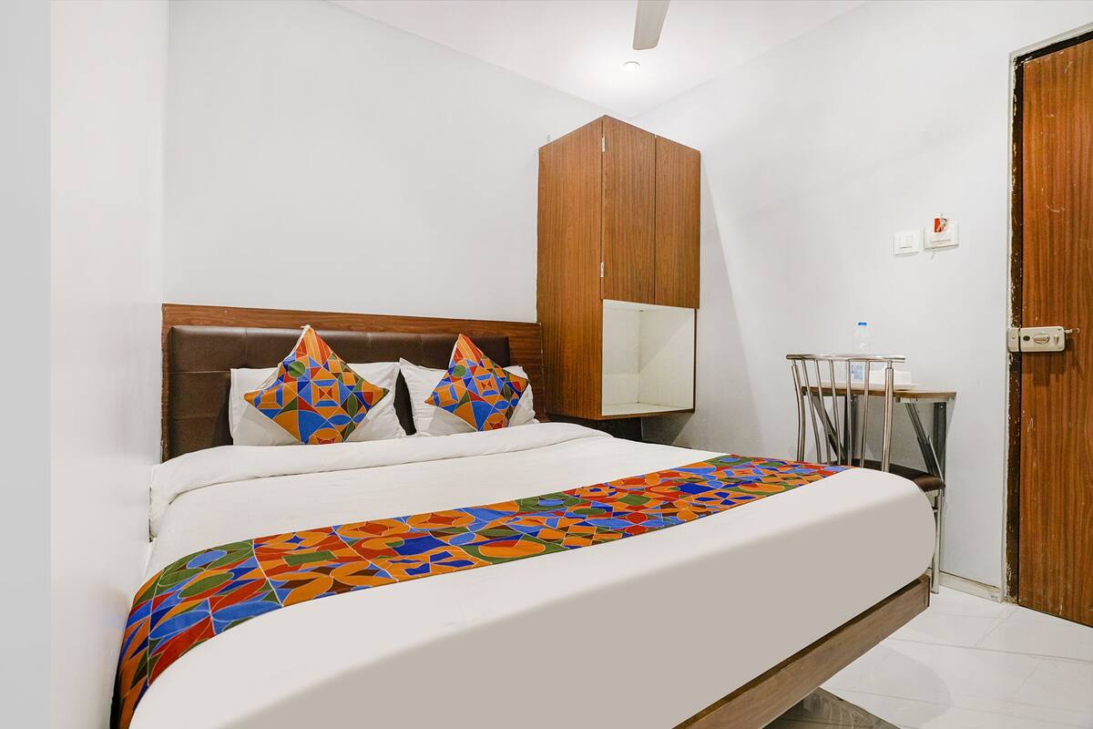 A bedroom with a bed, wooden wardrobe, and a small table with a chair.