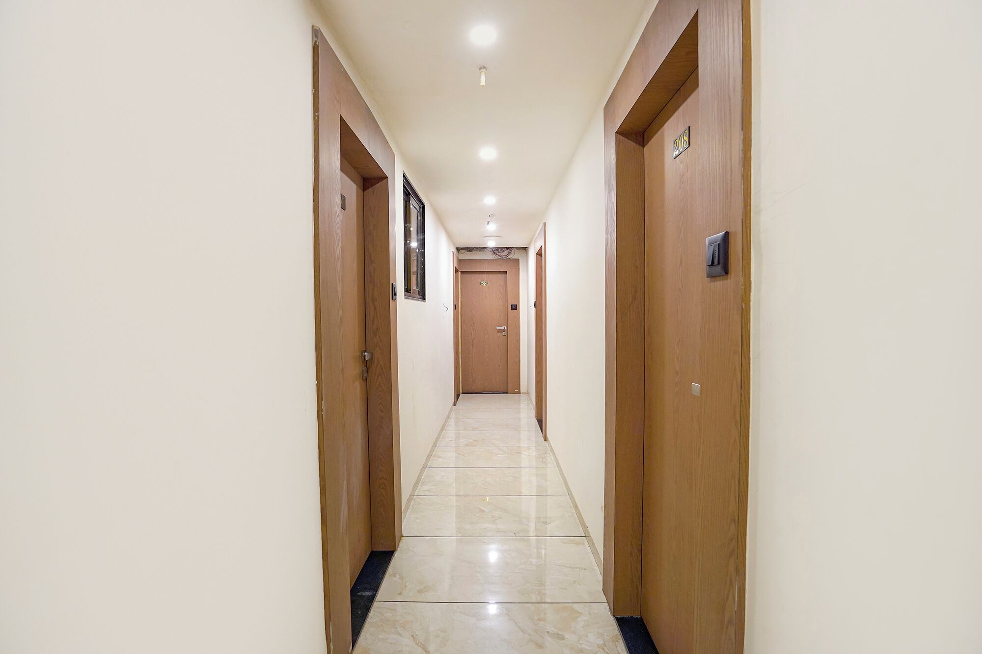 A corridor with wooden doors, a tiled floor, and a ceiling with recessed lighting.