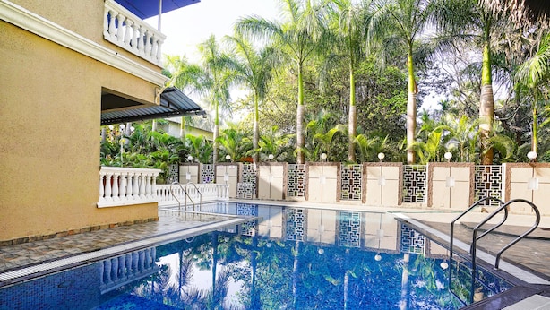 A swimming pool with a tiled deck, surrounded by palm trees and a building with a balcony.