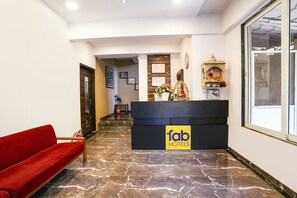 Un hall d'hôtel avec un sol en marbre, un canapé rouge, un comptoir d'accueil orné d'une enseigne indiquant « fab hotels », et un petit autel décoratif.