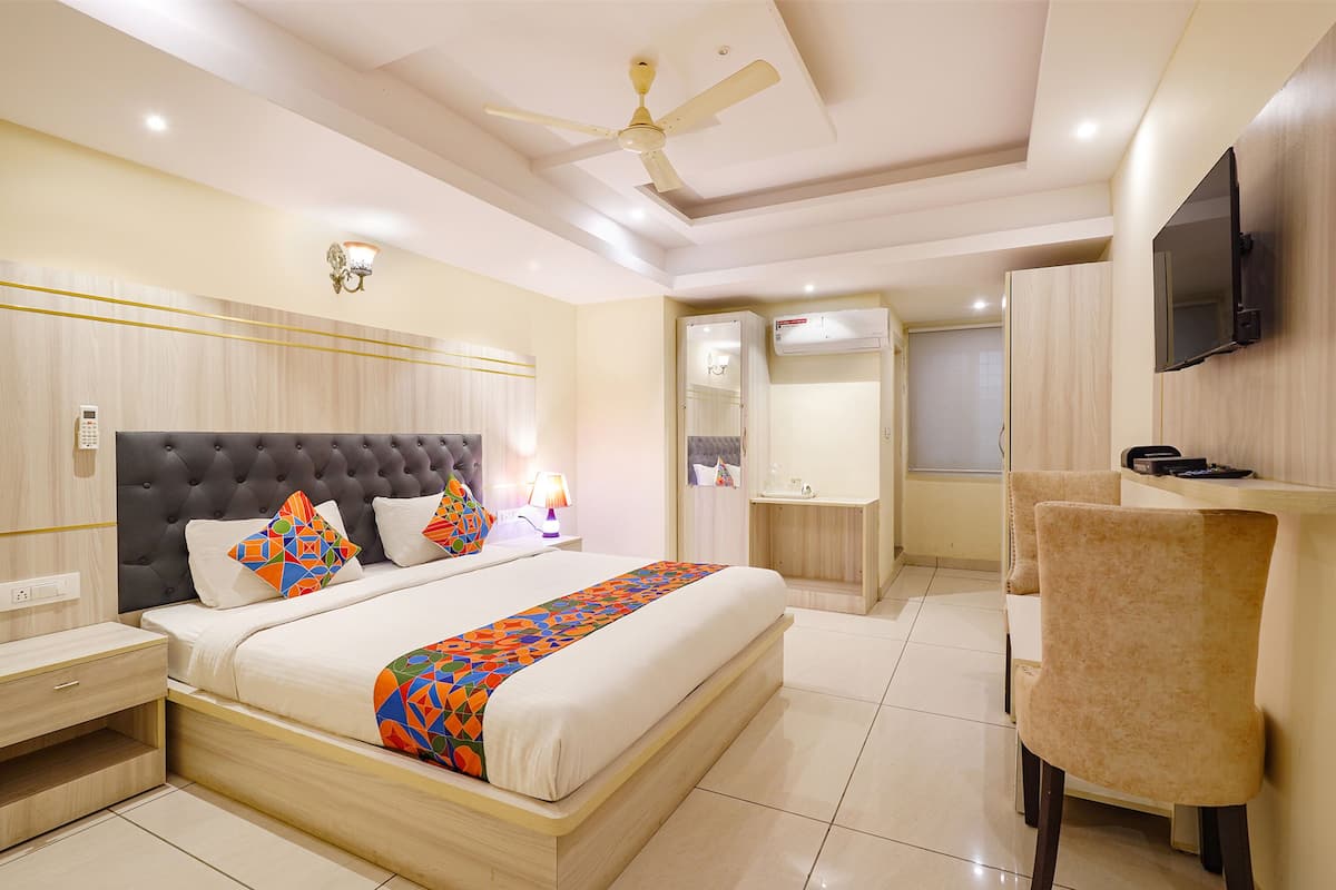 A hotel room with a large bed, a desk, a chair, a ceiling fan, a TV, and a bathroom with a shower and toilet.