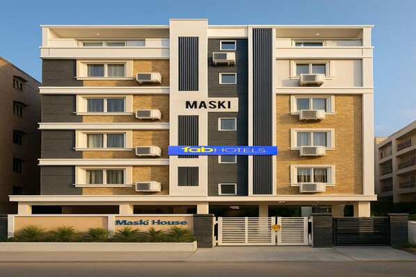 Ein mehrstöckiges Hotelgebäude namens "Maski House" mit modernem architektonischen Design, das Klimaanlagen in jeder Etage und einen verschlossenen Eingang aufweist.