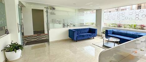 A modern lobby with a blue sofa, a glass coffee table, and a potted plant.