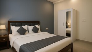 A neatly made bed with a dark headboard, a bedside lamp, and a wardrobe with a mirror. - Fabhotel Maski Suites (Hyderabad)