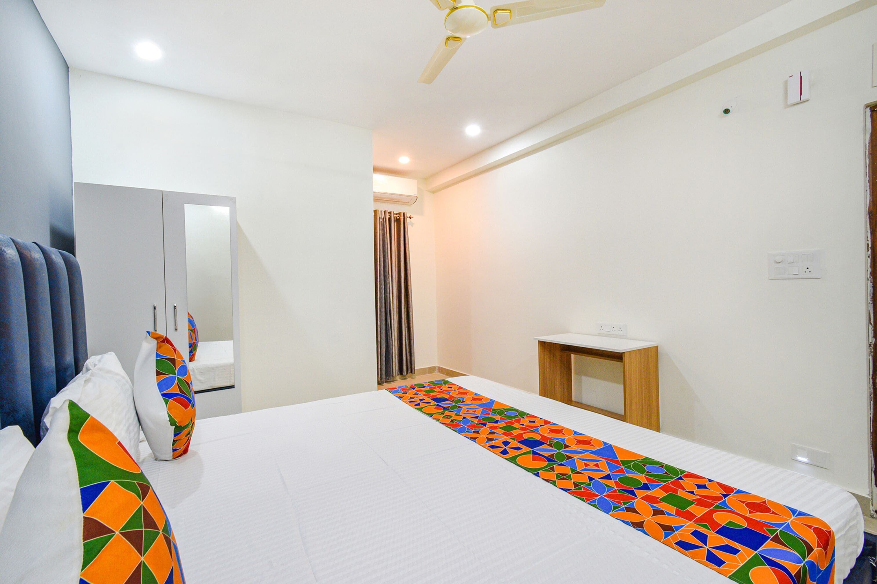 A hotel room with a bed, a bedside table, a mirror, and a ceiling fan.